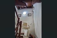 Beige stairlift moving downwards along a wooden staircase